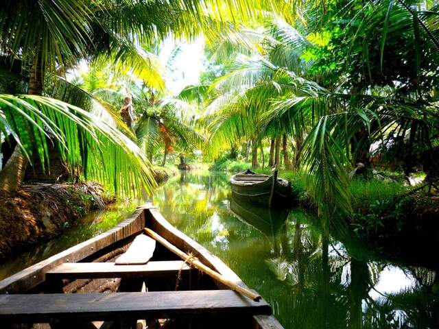 Ein Holzboot gleitet durch einen Kanal in den Backwaters in Südindien