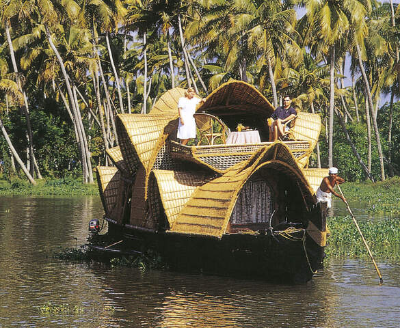 Ein großes Holzboot mit Touristen auf dem Sonnendeck fährt durch die Backwaters in Kerala